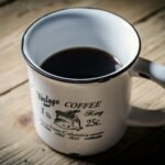 A vintage coffee mug with black coffee on a wooden table.