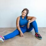Confident plus-size woman in blue activewear sitting on the floor, embracing self-love and body positivity.